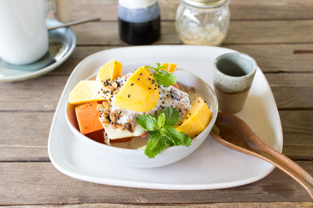 Mango, papaya, melon and pineapple fruit salad served with yogurt, milk, honey, sesame seeds and muesli. Porcelain bowl, plate and spoon are handmade.の写真素材