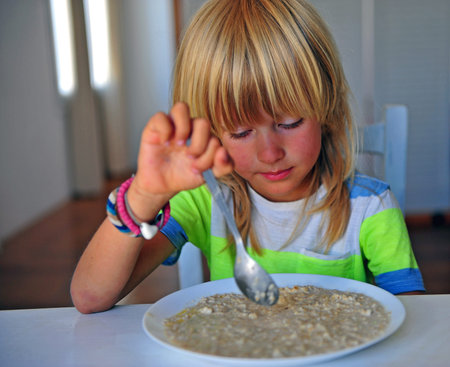 Boy with long hair having porridge on breakfastの写真素材