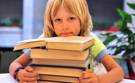 Adorable boy with books sitting in libraryの写真素材