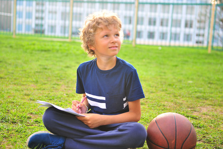 Boy with paper and basketball sitting on the grass outdoorsの写真素材