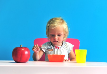 Baby eating her breakfast on blue backgroundの写真素材