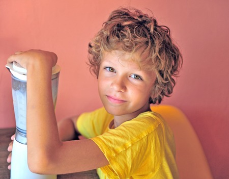 Portrair of a happy boy making milk shake for himself sitting at kitchen, adorable caucasian kid with shaggy hairの写真素材