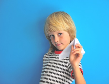 Portrait of joyful blonde boy holding paper airplane at the blue wallの写真素材