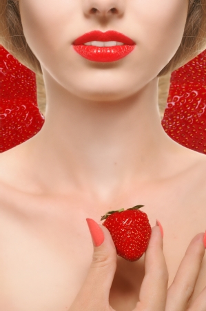 the lower part of the girl's face with red lips and a strawberry in hand on strawberry backgroundの写真素材