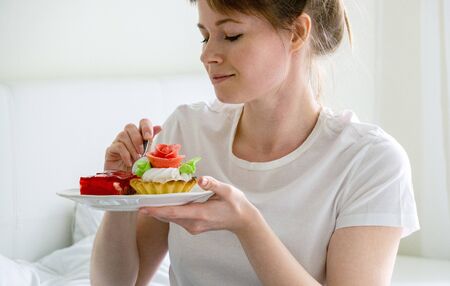 Woman sitting on the bed and eating cakesの写真素材