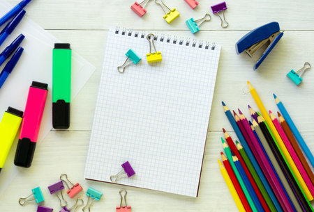 Blank notebook with various stationery on a white wooden background.