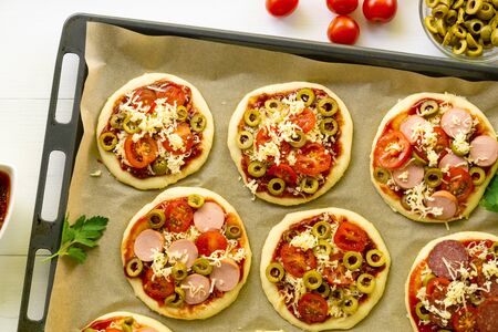 Raw mini pizza with sausages and tomatoes on a baking sheet.の写真素材