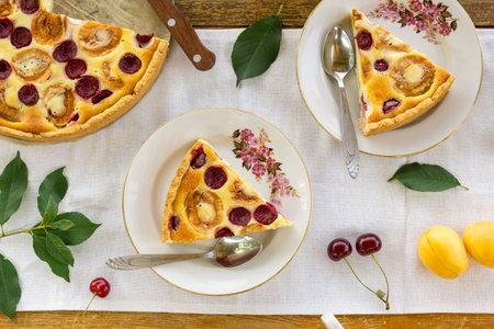 Pieces of summer fruit pie with sour cream filling, apricots and cherries on a white background.