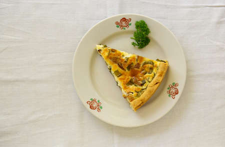 Piece of quiche with chanterelles, herbs and cheese on a white plateの写真素材
