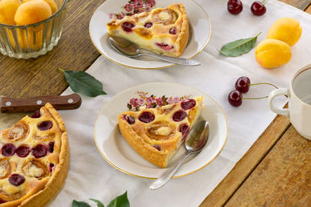 Pieces of summer fruit pie with sour cream filling, apricots and cherries on a wooden table.の写真素材