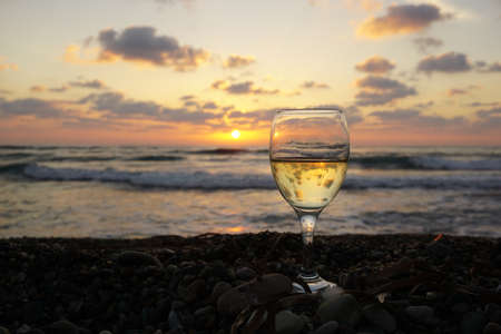 Glass of white wine on the pebble beach at sunset backgroundの写真素材