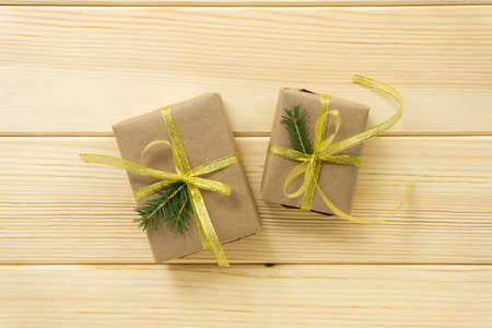 Holiday gift boxes wrapped in craft paper with golden ribbon and fir branches on a light wooden backgroundの写真素材