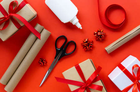 Christmas flat lay of gift boxes with wrapping craft paper, scissors, glue and decorations on a red backgroundの写真素材