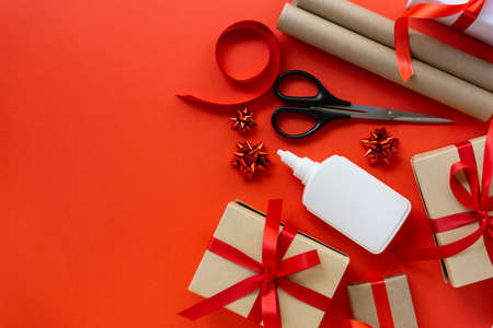 Christmas flat lay of gift boxes with wrapping craft paper, scissors, glue and decorations on red background, copyspaceの写真素材