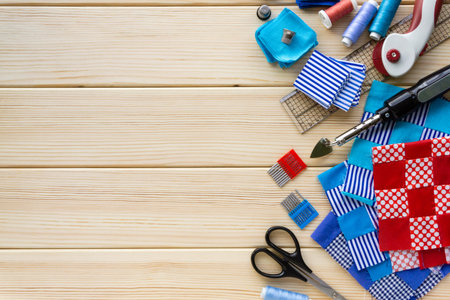 Items for patchwork. Pieces of fabric and sewing accessories on a wooden background. Space for text.