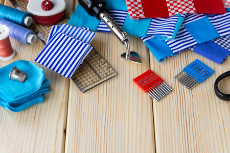 Items for patchwork. Pieces of fabric and sewing accessories on a wooden background.