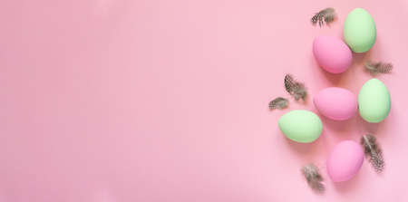 Pink and green easter eggs with feathers on pastel background, space for textの写真素材