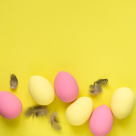 Flat lay of yellow and pink painted easter eggs with feathers on colored backgroundの写真素材