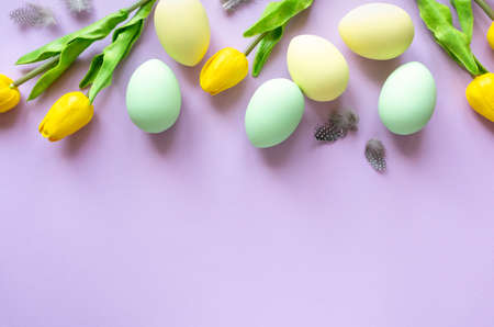 Easter flat lay. Painted eggs with tulips and feathers on lilac background, space for textの写真素材