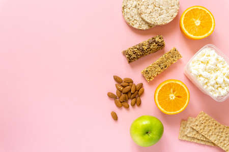 Flat lay of healthy snacks. Fruits, muesli bars, crispbreads, cottage cheese and nuts on pink background, space for textの写真素材