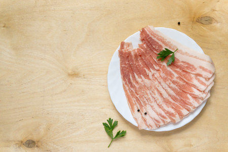 Raw bacon slices with parsley and pepper on wooden background, top viewの写真素材