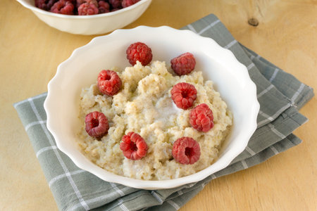Milk barley porridge with butter and raspberries in white bowl on wooden background.の写真素材