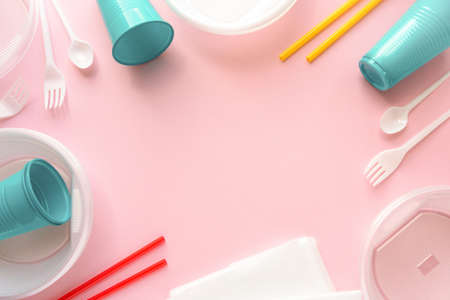 Frame of various disposable plastic tableware on pink background, space for textの写真素材