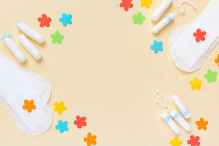 Flat lay of female menstrual supplies. Tampons and pads with paper flowers on beige backgroundの写真素材