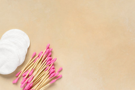 Cotton pads and colored ear sticks on beige background, space for text