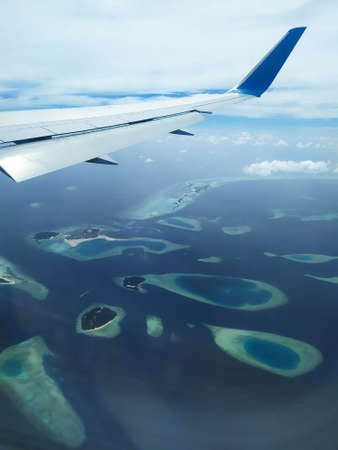 Scenery from airplane s window. A wing of airplane, white clouds, blue sky and Maldives islands.の写真素材