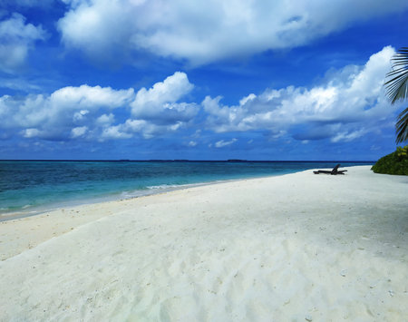 Maldives, the deserted beach with empty sunbeds. A white sand, turquoise ocean and a blue sky.