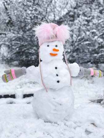 A snowman in a pink hat and gloves stands next to a snow-covered tree. Merry Christmas and Happy new...