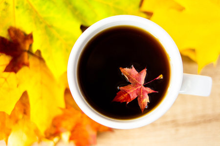 White cup of tea and autumn maple leaves on wooden background. The concept of calm, relaxation and...