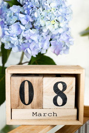 Close up a wooden calendar with the date March 8 on a blue hydrangea background. International...