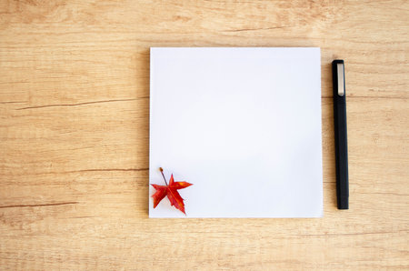 Notepad and pen lie on a wooden background with red autumn leave. Back to school.