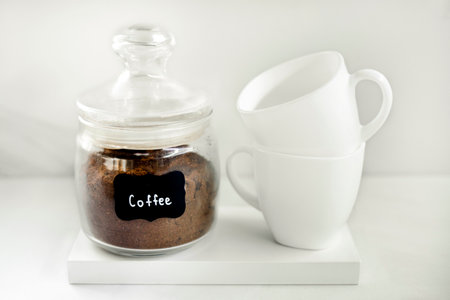 Freshly ground coffee in a glass container with two white caps on the white background. Breakfast coffee concept. Process of making coffee at home.の写真素材