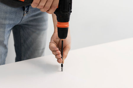 A young craftsman assembles furniture fittings. Screwing the confirmat close-up. Professional furniture assembling. Installation of new furniture. Furniture assembly.の写真素材