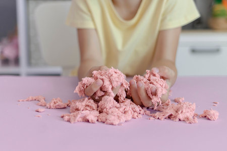 The kid plays with kinetic sand stirring it in her hands. Close-up view of childrens hands with pink kinetic sand.の写真素材