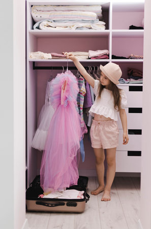 A little girl of European appearance puts things in a suitcase in a dressing room. Preparation, getting ready for a vacation trip.の写真素材