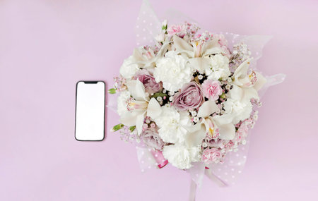 A phone with a white screen lies near the flowers isolated on pink background. The concept of online...