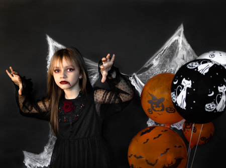 A little girl dressed in a red and black costume as a vampire on Halloween is isolated on a black background with cobwebs. Halloween concept.の写真素材