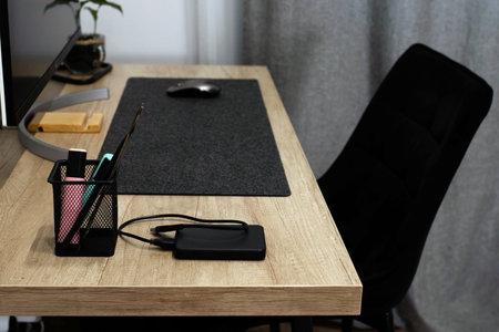 Minimalist home office desk with computer, external hard drive, and stationery. Modern wooden table...