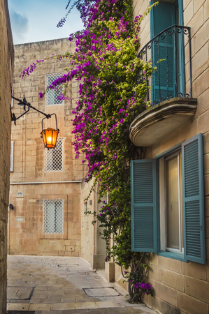 Mdina, Malta: traditional Maltese house with artistic balcony and windows, covered with bright purple flowers on the limestone wall and lantern lightsの写真素材