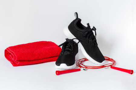 Black sports running shoes with white sole, red jumping rope and red towel isolated on white background. Concept of fitness and healthy lifestyleの写真素材