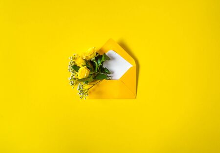 Open envelope with yellow roses and small white flowers Gypsophila on yellow background. Top view, flat lay. Concept of sending greetings, love, friendship and joy.の写真素材