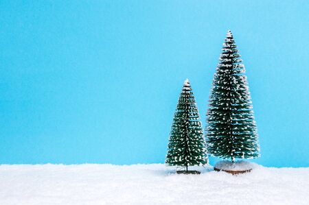 Winter landscape theme with two small Christmas trees on snow against blue paper background. Christmas holiday and winter concept. Copy-space for text.の写真素材