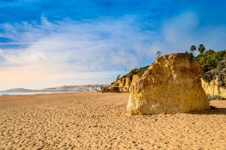 Wide sandy beach Praia de Albufeira and cliffs in resort village in Algarve, Portugal at sunset. Albufeira is popular summer touristic destination with scenic nature and beautiful seascape.の写真素材