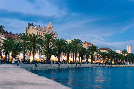 Split, Croatia - May 21, 2019: Riva Promenade with palm trees, lights and tourists sitting on steps and watching the sea at dusk in the evening. Popular touristic destinationのeditorial素材