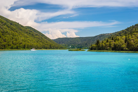 Green hills with forest around Krka river in beautiful Krka National Park, Croatia. Touristic boats...