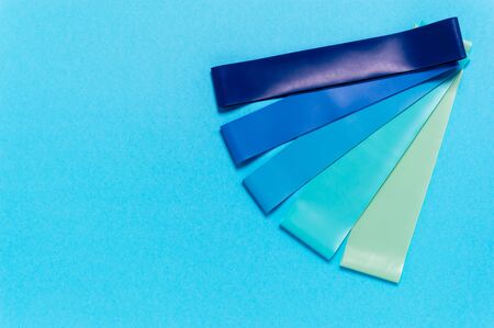 Set of elastic rubber resistance bands in blue, turquoise and green on blue background. Equipment for sports or workout at home. Fitness and rehabilitation gear. Flat layの写真素材